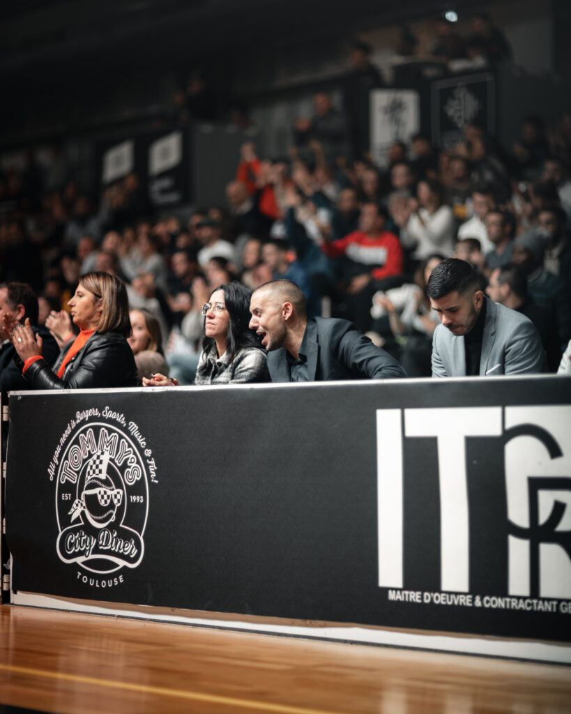 Public assis autour d'un terrain de basket en train de crier pour célébrer une action de jeu